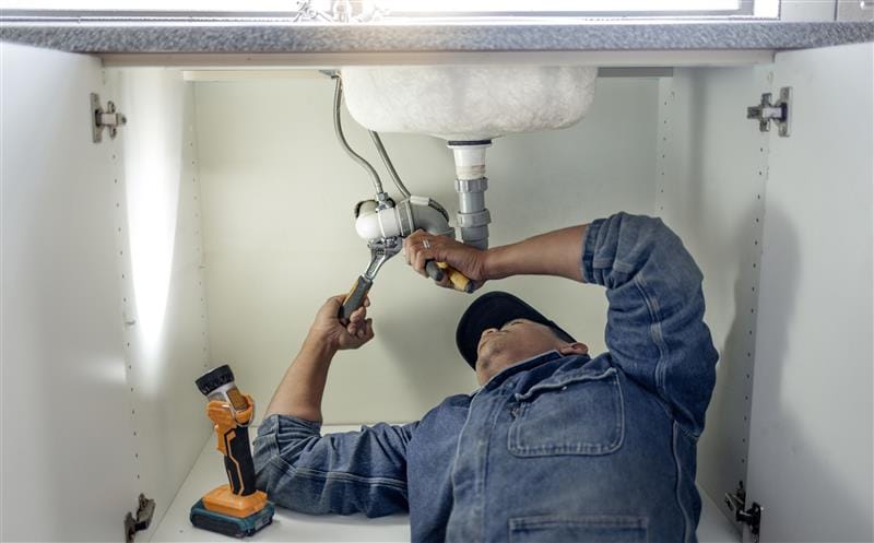 Plumber repairing pipes beneath a bathroom sink in Claremont